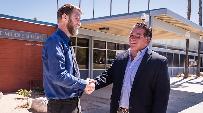 Two men shaking hands in front of school