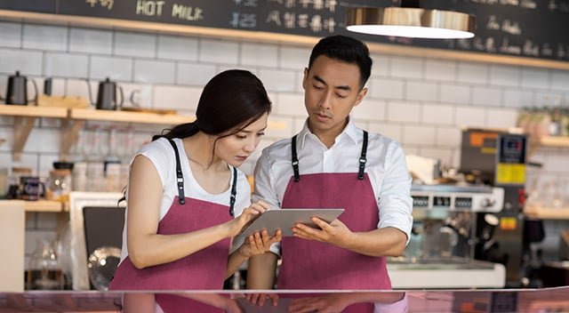 Two café employees looking at a tablet behind a counter.