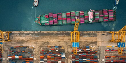 An overhead view of brightly colored shipping containers being unloaded by a yellow crane at a port.