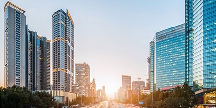 A street-level scene of city skyscrapers, with sunrise light appearing over the horizon.
