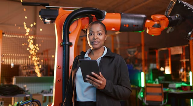 Black woman holding black tablet with orange robotic arm in the background
