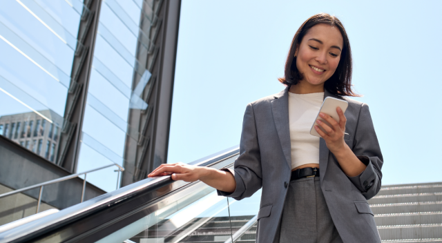 A smiling government employee uses her smartphone while descending an outdoor staircase.