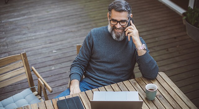 A government employee takes a work call from his patio while seated in front of his tablet and laptop.