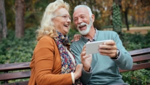 Two seniors laughing together while one of them holds a smartphone in front of them.