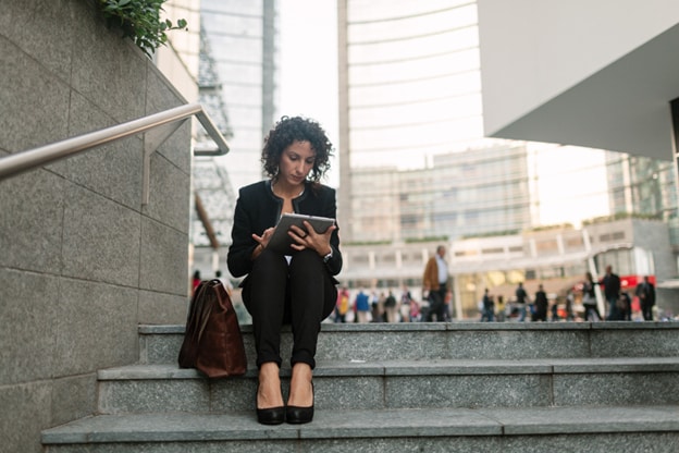 A woman working on tablet in city, sitting on some steps.