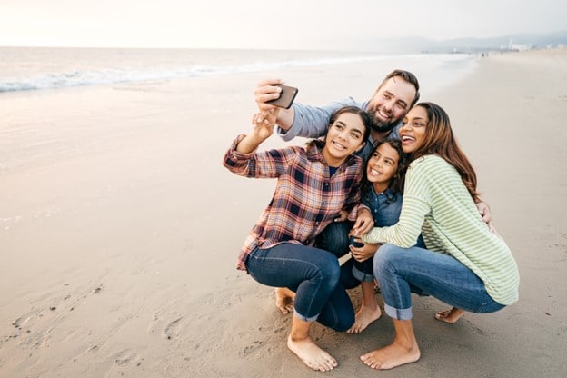 Two kids with parents taking a group selfie on the beach.