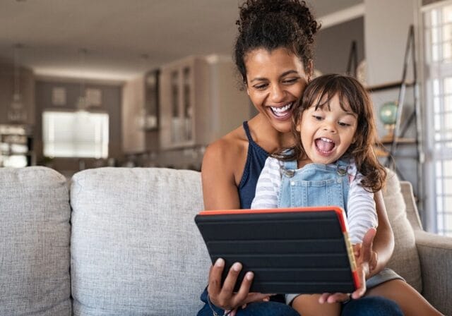 Mom and child sitting on a couch holding and smiling at an ipad
