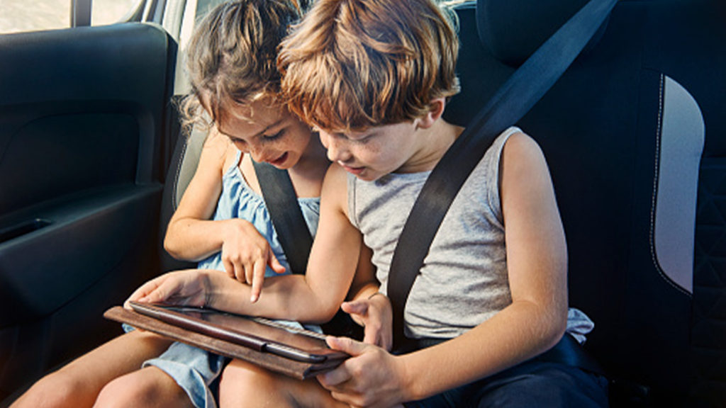 Two children in the backseat of a car watching a tablet.
