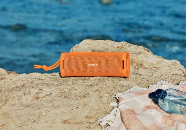 A portable speaker being used on the beach near water.