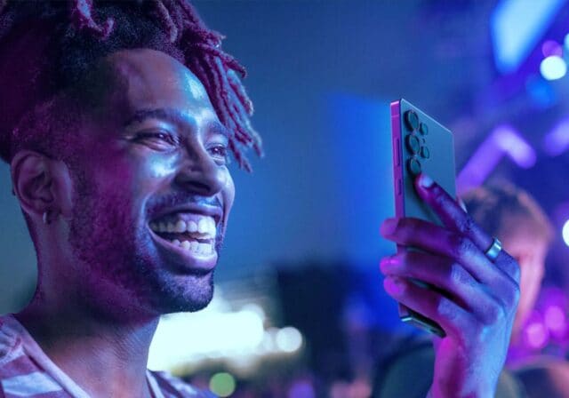A person holding a phone in their hand and smiling at it.