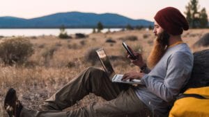 A person sat outdoors with a phone and a laptop.