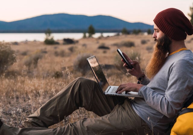 A person sat outdoors with a phone and a laptop.