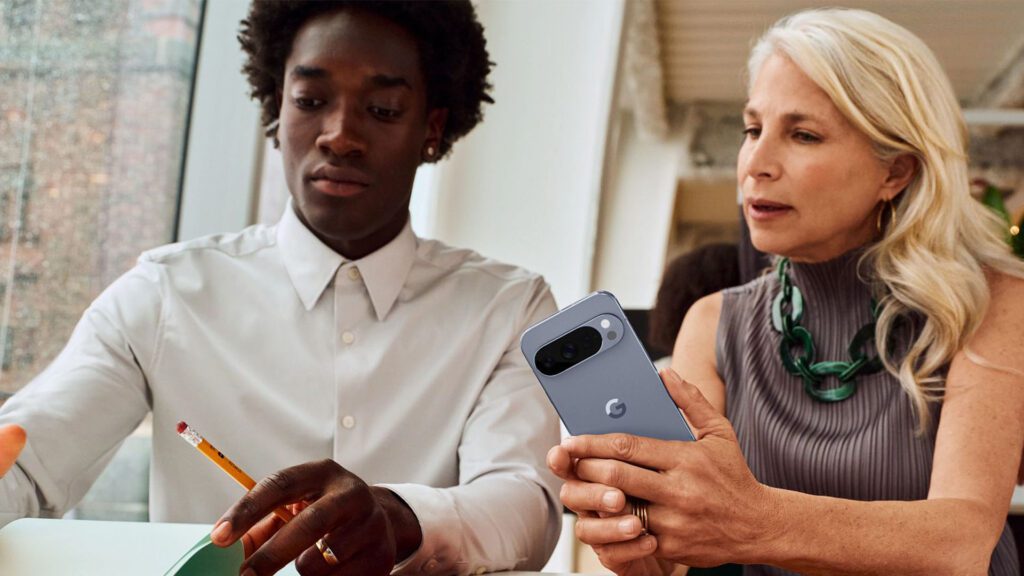 Two people sitting next to each other in a business setting with one holding the Google Pixel 10 Pro.