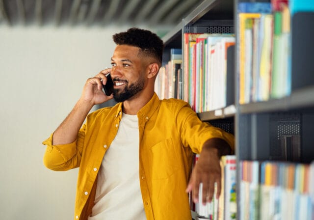 Young-university-student-indoors-in-library-using-smartphone