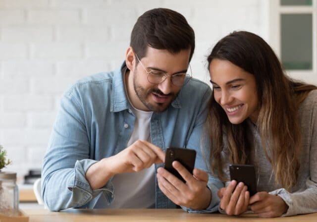 A smiling couple looking at their mobile devices.