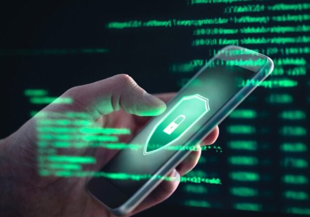 A person holding an iPhone with a green shield and padlock logo on the screen.