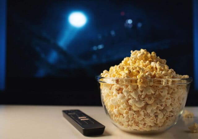 Image of popcorn and a remote in front of a screen.