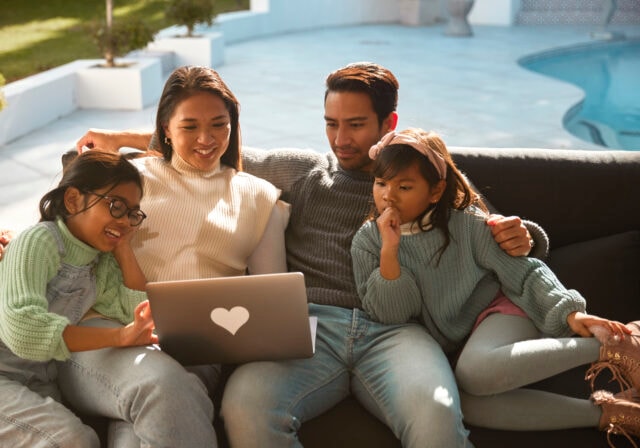 A joyful family gathers on the outdoor sofa, sharing smiles and laughter as they huddle around a computer screen, creating cherished memories together.