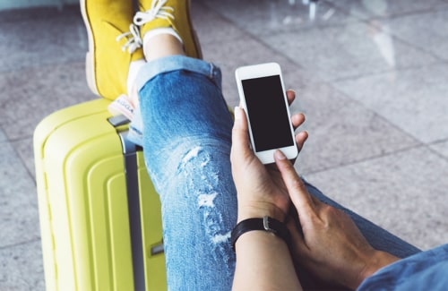 Person ready for travel with feet on roller bag uses smartphone.