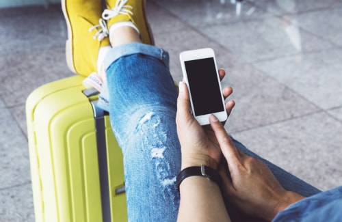 Person ready for travel with feet on roller bag uses smartphone.