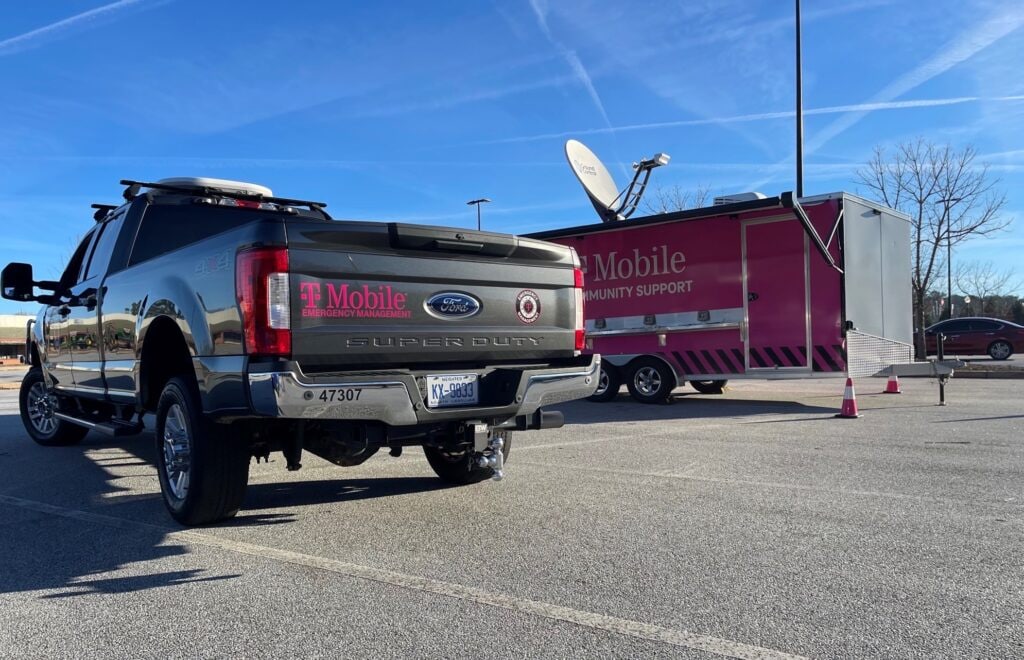 Two T-Mobile branded emergency response trucks in an open parking lot with blue skies