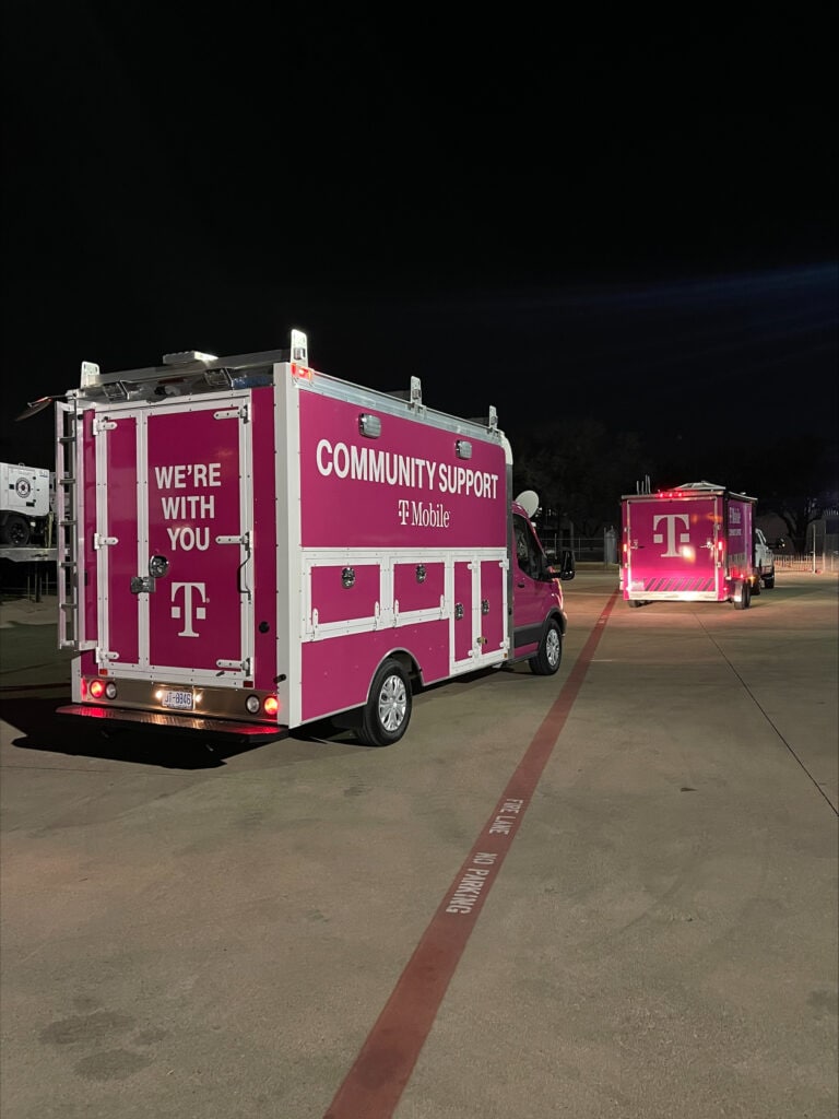 Two T-Mobile branded emergency response trucks in an open parking lot in the night time with dark skies
