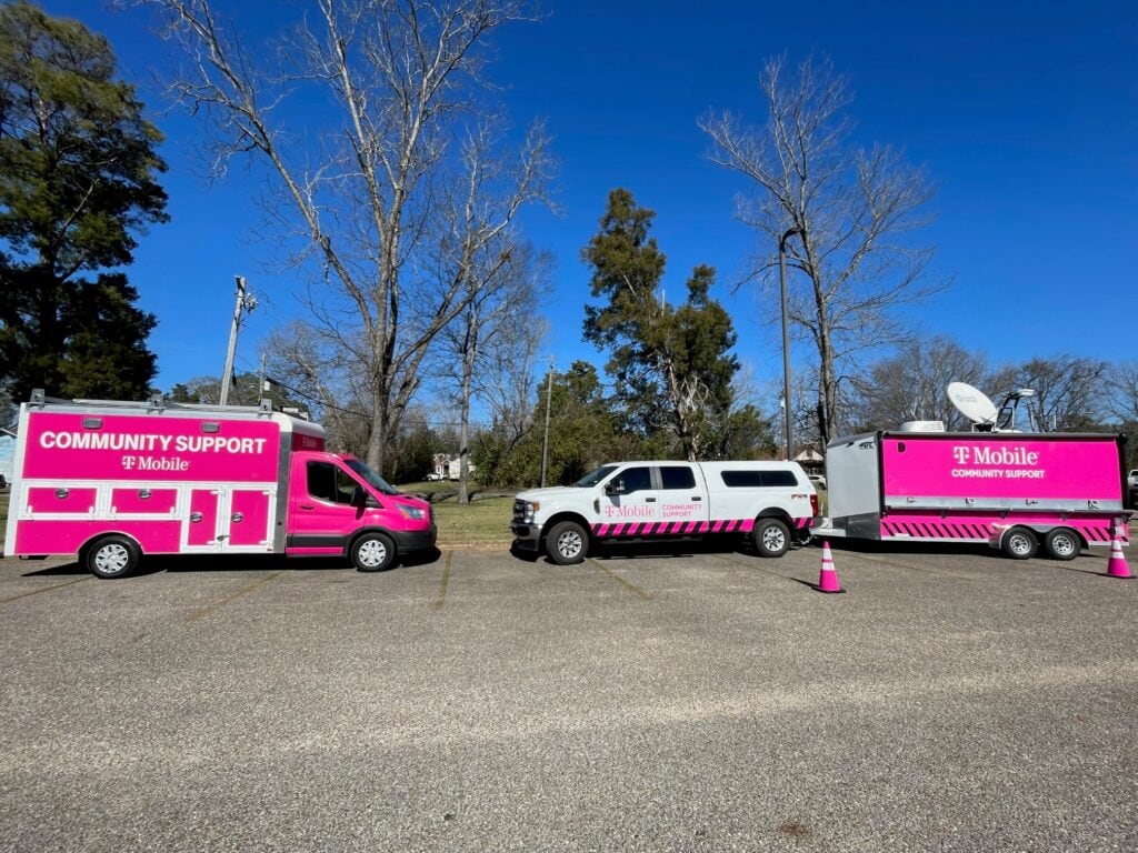 Two T-Mobile branded emergency response trucks in an open parking lot with blue skies and trees in the background