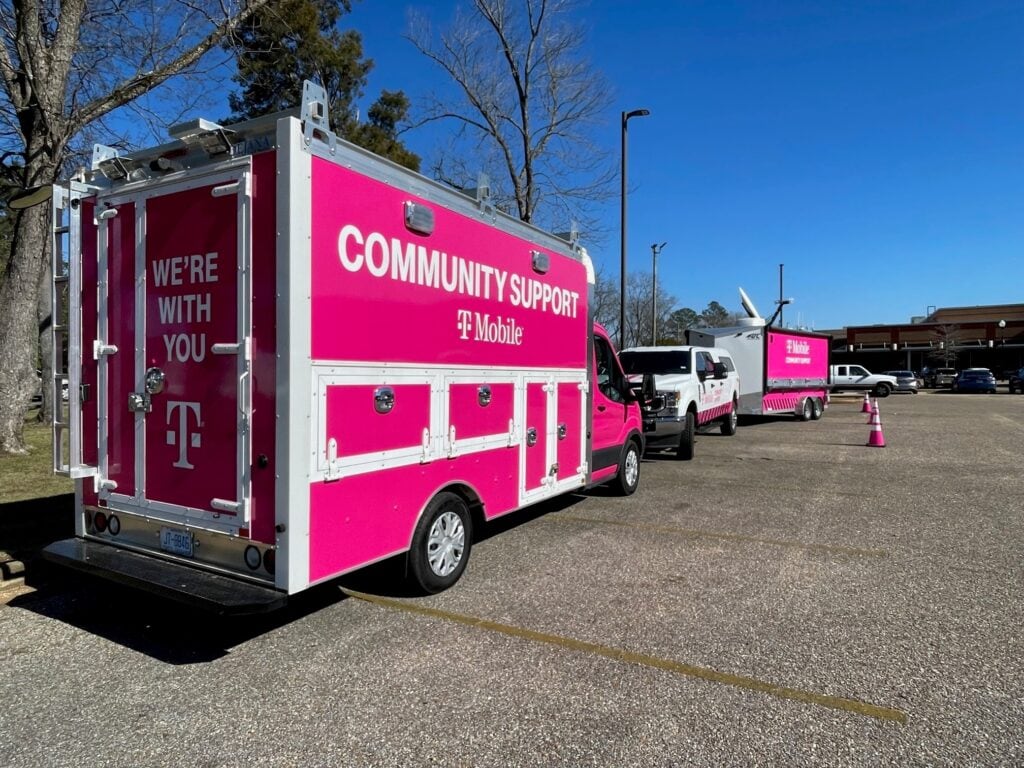 Two T-Mobile branded emergency response trucks in an open parking lot with blue skies and trees in the background