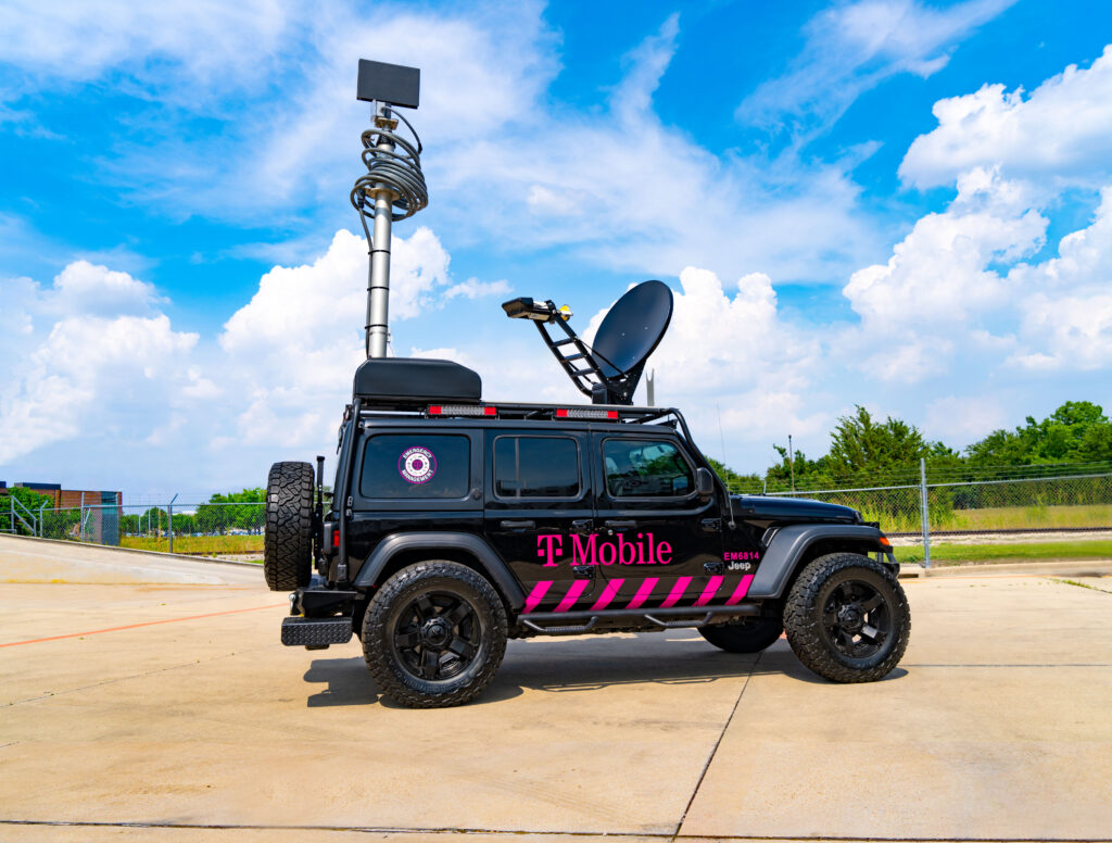 T-Mobile logo branded all-terrain vehicle with mounted satellite equipment extended. Vehicle is parked outdoors