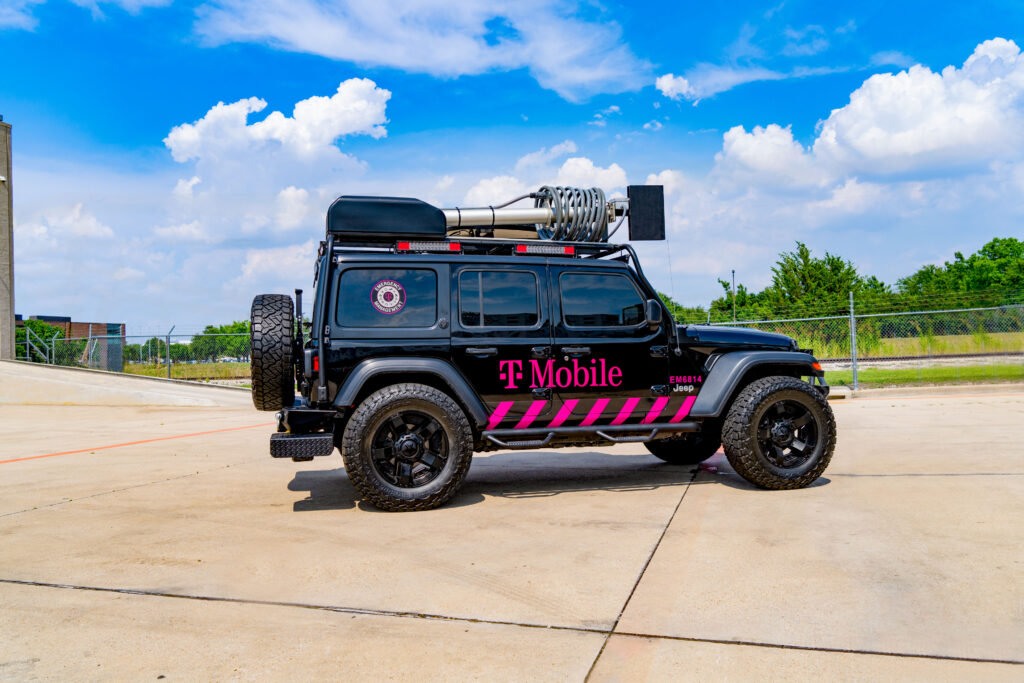 Un vehículo todoterreno con el logotipo de T-Mobile tiene un equipo satelital que está replegado para mostrar su portabilidad. El vehículo está estacionado al aire libre