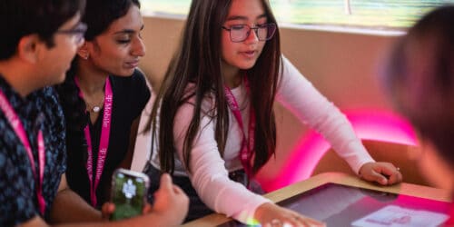 Two girls and one boy in middle school sitting around a table with a touch screen surface at the Changemaker Challenge lab