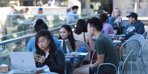 students sitting at cafe tables with laptops open in front of them.
