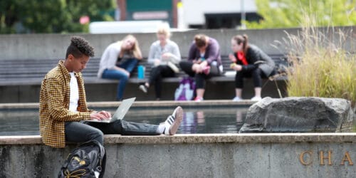 Students sit on concrete steps with various laptops open.