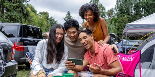 A group of four people sitting in a parking lot watching a video on their cell phone.