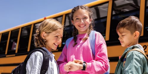 three kids getting ready to go back to school using new syncup kids 2 watch by t-mobile standing in front of a school bus