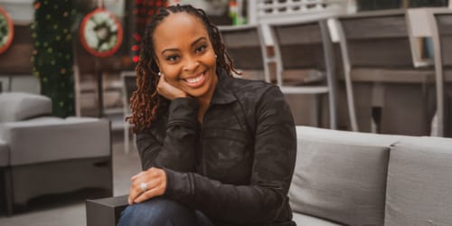 Image depicts A'Naja Newsome, Ph.D., sitting on a couch with her hand on her face
