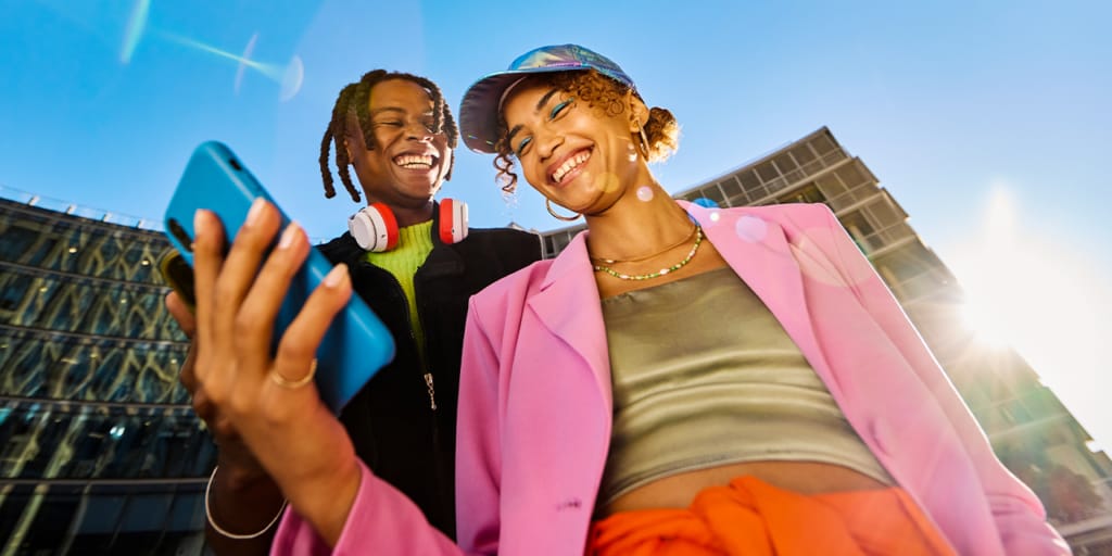 Two young people smiling. The young woman is holding a blue phone. 