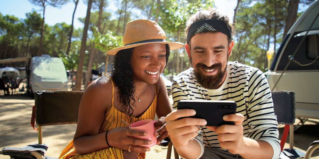 Two people smiling at a phone screen at camping site. 