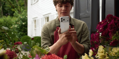 Man looks at iPhone 17 surrounded by flowers