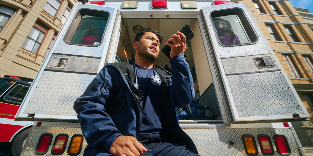 An emergency medical technician (EMT) sitting on the back of an ambulance and talking on the phone