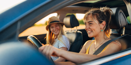 two women smiling while driving in a car
