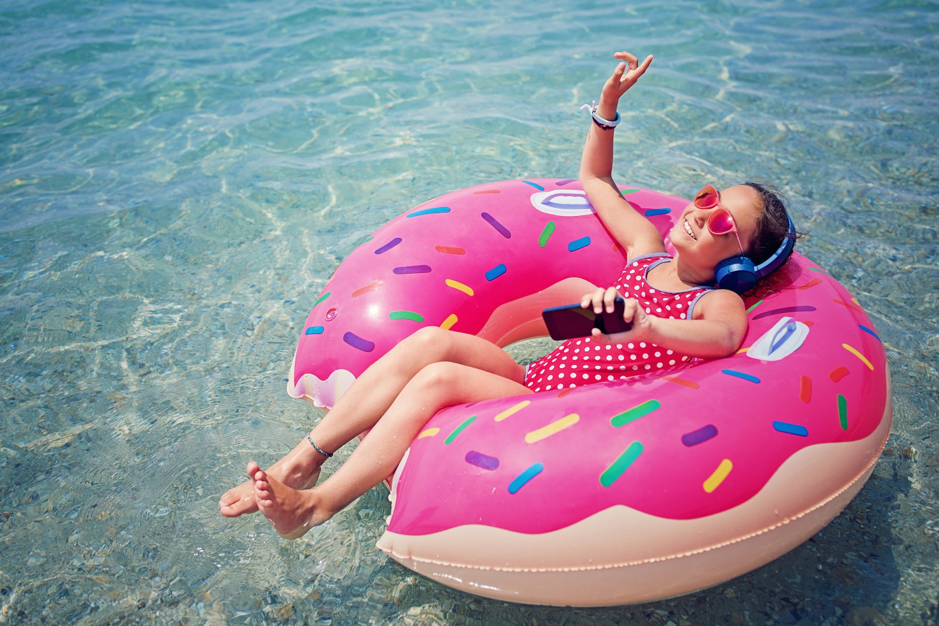 A girl sits on a pool float listening to music.