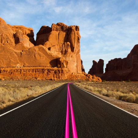 A desert highway with solid magenta center lines and mesas in the distance.